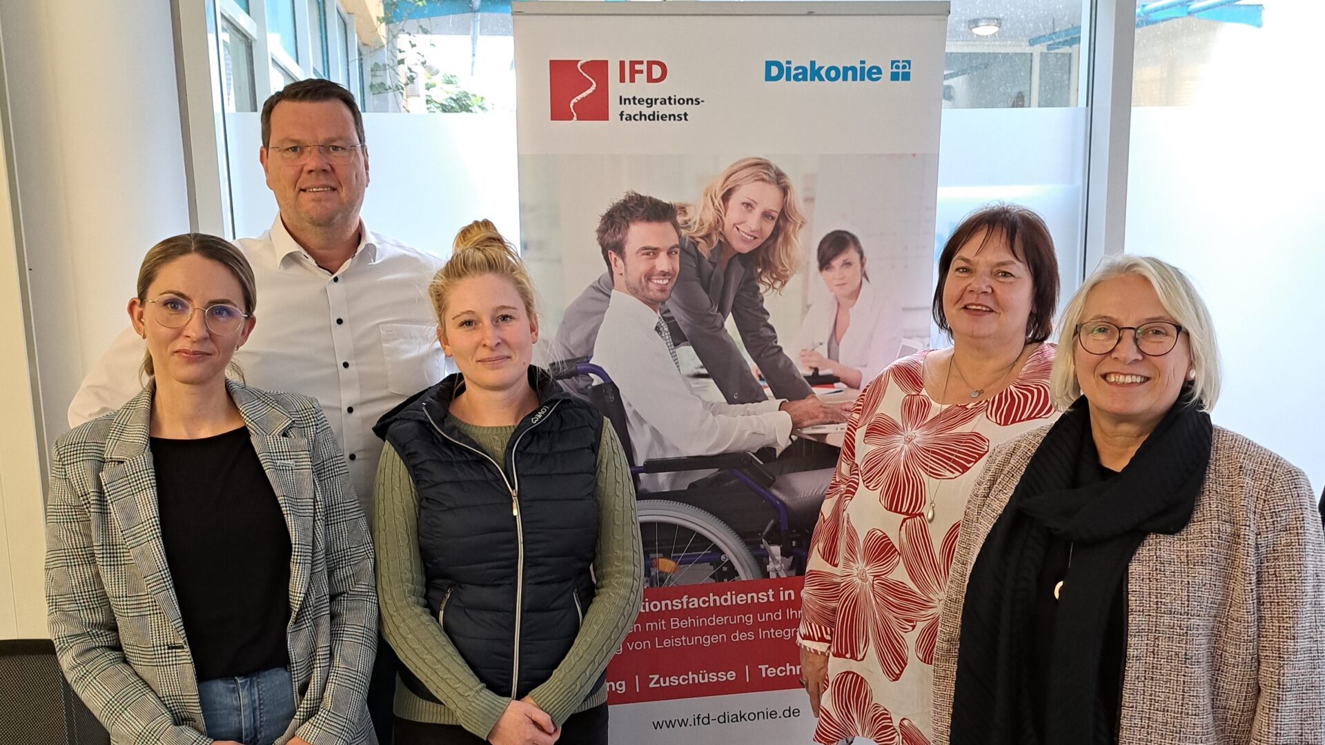 Ein Mann und vier Frauen stehen vor einem Plakat der Diakonie