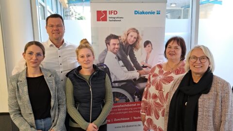 Ein Mann und vier Frauen stehen vor einem Plakat der Diakonie